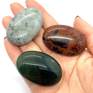 Macro shot of polished oval labradorite and mahogany obsidian palm stones held in hand