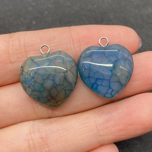 Detail of 20mm heart-shaped dragon vein agate pendants held by fingers for scale
