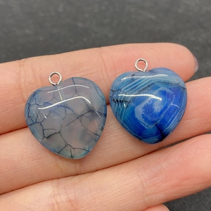 Detail shot of heart-shaped striped agate pendants held by hand to show 20mm size