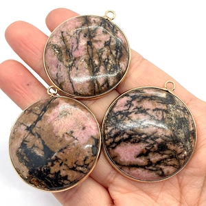 Trois pendentifs en rhodonite avec bordure dorée présentés à la main sur fond blanc