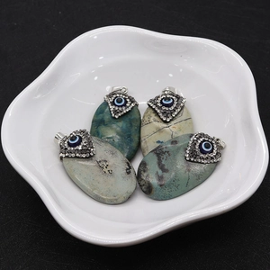 Macro view of natural stone oval pendants with evil eye inlay in a white ceramic dish