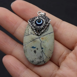Close-up of natural stone oval pendant with evil eye charm and rhinestone inlay
