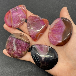 Macro detail of natural striped agate pendants in teardrop and oval shapes held in hand