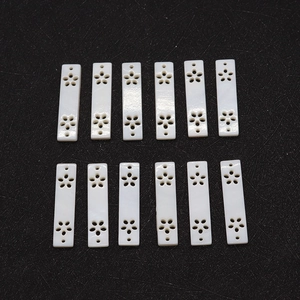 Detailed view of 12 carved rectangle white shell charms with floral cutout patterns