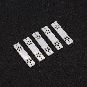 Macro view of five cream white rectangular shell pendants with hollow floral carvings