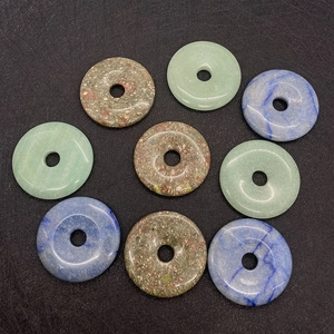 Flat lay of 50mm natural aventurine and sodalite stone donut pendants on dark surface