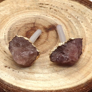 Makroaufnahme von rosa Quarz-Ohrringen mit Goldrand auf einem Holzsockel