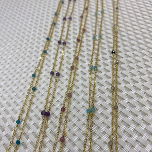 Detail of gold metal oval link chains featuring multi-colored faceted round stone beads