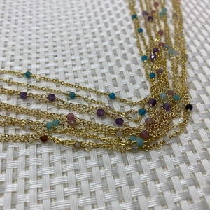 Detail of copper gold-plated chain with small colorful natural stone beads on a white mat