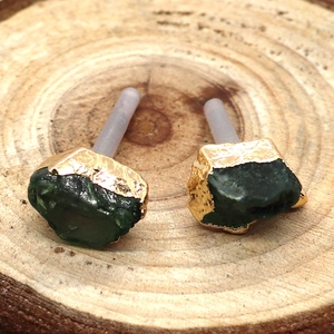 Dettaglio degli orecchini in pietra grezza verde con bordi dorati su fondo in legno