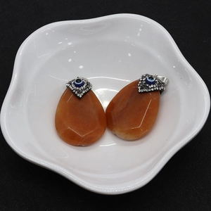 Detailed view of orange teardrop stone pendants with evil eye motif in a white ceramic tray