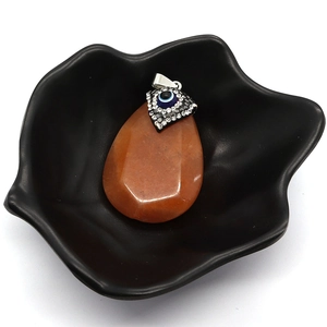 Teardrop natural stone pendant with evil eye charm in an artistic black ceramic dish