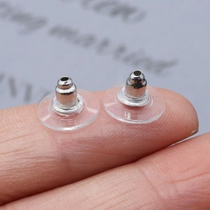 Close-up of silver bullet ear studs with plastic pads held between fingers