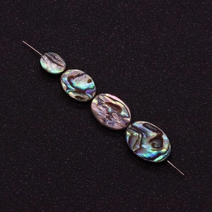 Vue rapprochée de perles d'ormeaux ovales irisées sur fil avec reflets métalliques
