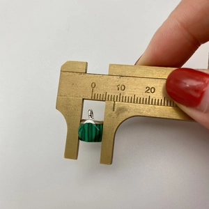 Measuring the width of a green malachite faceted pendant with a brass caliper tool