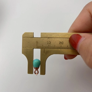 Macro shot of an 8mm turquoise teardrop pendant measured with a brass caliper scale