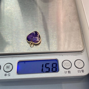 Macro-opname van een paarse hartvormige stenen hanger met gouden rand die 1,58g weegt op schaal