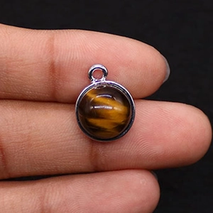 Detail view of round tiger eye stone pendant with silver metal bezel held by fingers