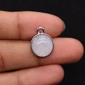 Macro detail of a round white crystal pendant with silver bezel held by fingers