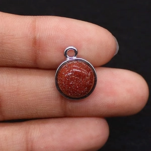 Macro shot of 10mm round gold sandstone pendant with silver plated bezel held by fingers