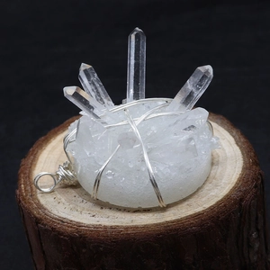 Detailed view of white crystal cluster pendant with silver wire wrap on wooden base