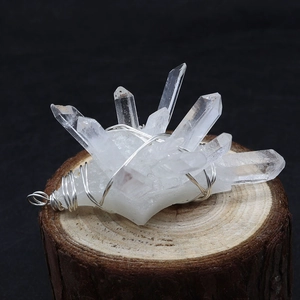 Macro shot of clear white crystal pendant with silver wire wrap on wooden base
