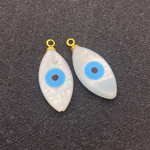 Detailed close-up of natural shell evil eye charms with golden loops on a black background