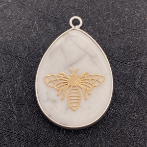 Macro shot of waterdrop white stone pendant with gold bee inlay and silver frame