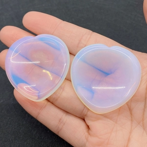 Macro shot of two heart-shaped opal worry stones with soft blue glow on a palm