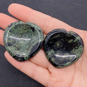 Close-up of heart-shaped polished malachite stones held in hand for size perspective