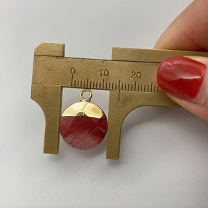 Detailed measurement of circular faceted watermelon crystal pendant with brass caliper
