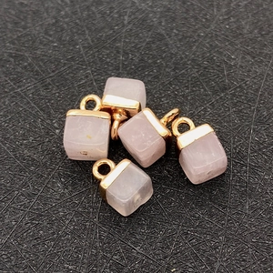 Macro view of five pink rose quartz cube pendants with gold metal bail on black background