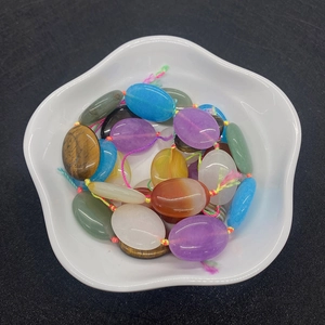 Polished oval natural stone beads in a white ceramic bowl for DIY jewelry making