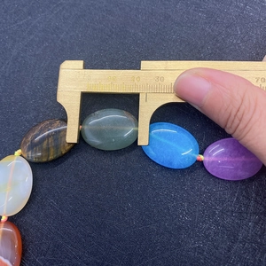 Measuring 25mm oval natural stone beads with a yellow caliper on a dark background