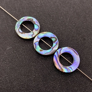 Detailed view of iridescent abalone shell circular hollow beads showing natural colors