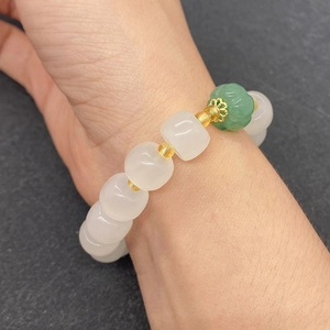 Dettaglio macro di perline di giada bianca e pietra verde intagliata su bracciale oro