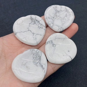 Detailed close-up of four polished heart-shaped howlite stones held in hand for scale