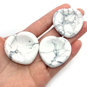 White turquoise heart-shaped thumb stone for stress relief held in hand on white background
