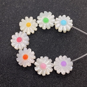 Macro shot of 10-12mm daisy shell beads with colorful enamel centers on grey background
