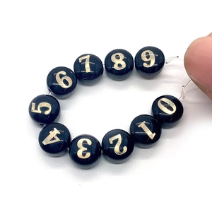 Dettaglio di perle in conchiglia nera con numeri dorati per gioielli e bracciali fai-da-te