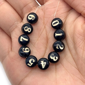 Primo piano di perline di conchiglia nere con numeri d'oro 0-9 per gioielli DIY