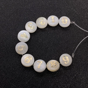Close-up of 8mm white shell beads with golden Arabic numbers for DIY jewelry making