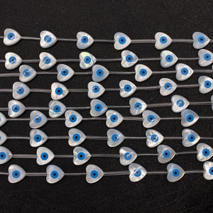 Close-up of heart-shaped shell beads with evil eye pattern on a black background