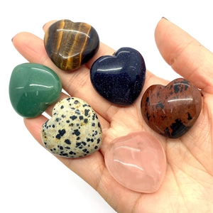 Polished heart-shaped natural gemstones in hand showing textures of tiger eye and quartz