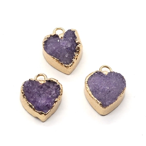 Vista macro di tre ciondoli in cristallo druzy viola a forma di cuore con bordi dorati