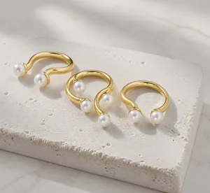 Primer plano de un anillo abierto dorado con dos perlas blancas sobre un fondo minimalista
