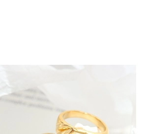 Detailed macro view of a gold-plated twisted texture ring on white fabric background