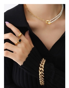 Close-up of golden paperclip chain necklace with freshwater pearls and bold rings