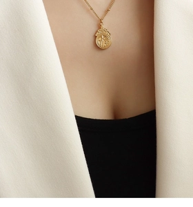Detalle de collar de acero de titanio dorado con colgante Fu sobre fondo de traje blanco