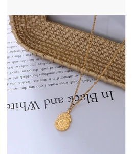Detalle del collar de acero inoxidable chapado en oro 18k con colgante Fu sobre carta